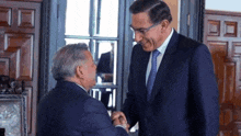 two men in suits are shaking hands and smiling