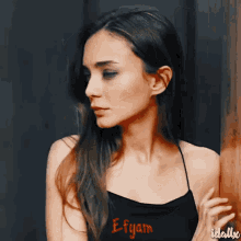 a woman leaning against a wall wearing a black top that says e-fyam
