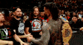 a man with a wrestling belt is shaking hands with another man in a crowd .