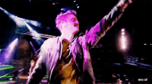 a man in a purple jacket is standing on a stage with his arms in the air ..