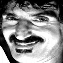 a close up of a man 's face with a mustache smiling .