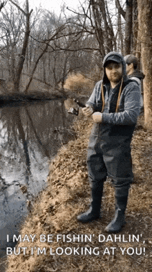 a man in waders is standing next to a river holding a fishing rod