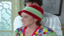a woman wearing a red hat and a green scarf stands next to a man