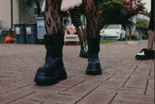 a person wearing a pair of black boots with orange soles walking on a brick sidewalk
