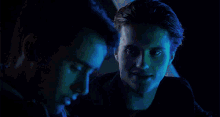 two men are looking at each other in a dark room with blue lights