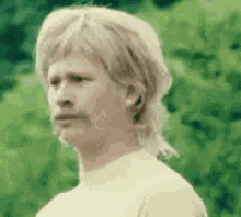 a man with a mullet and mustache is wearing a wig and looking at the camera .