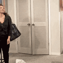 a woman is standing in front of a closet holding a black bag .