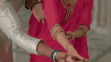 a woman in a pink dress is putting bracelets on a man 's wrist