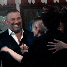 a man in a suit and white shirt is smiling and hugging a woman
