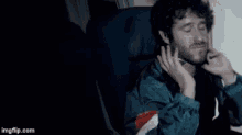 a man is sitting on an airplane with his eyes closed and talking on a cell phone .