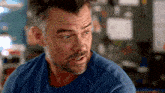 a man with a beard is wearing a blue shirt and looking at something .