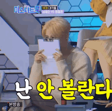 a man covering his face with a clipboard while sitting in a chair with korean writing on it