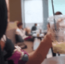 a person is holding a cup of coffee with a straw in front of a group of people sitting at tables .