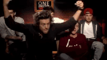 a group of men sitting in front of a one direction sign