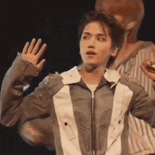 a man in a gray and white jacket is waving his hand .
