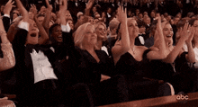 a crowd of people are sitting in a theatre applauding at an awards ceremony .