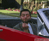 a man in a suit and tie is sticking his finger out of a car window .