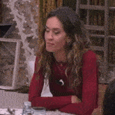 a woman wearing a red sweater is sitting at a table with her arms crossed .