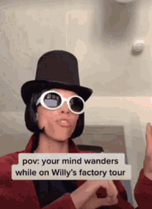 a man wearing a top hat and sunglasses is making a funny face while on willy 's factory tour .