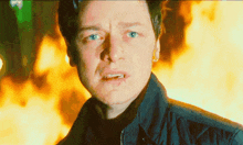 a close up of a man 's face with a fire behind him