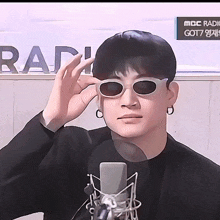 a man wearing sunglasses stands in front of a microphone