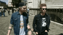 two men are walking down a sidewalk holding hands .