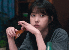 a woman in a grey shirt is eating a piece of meat