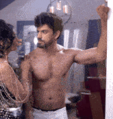 a shirtless man leans against a wall while a woman holds his shoulder