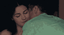a man and a woman are kissing in a dark room . the man is wearing a green shirt .
