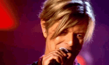 a close up of a man singing into a microphone with a purple background