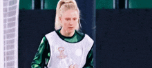 a woman is wearing a green and white soccer jersey and a white vest .