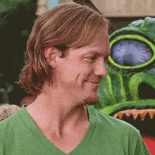 a man in a green shirt is smiling in front of a monster