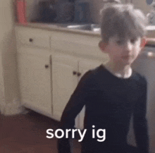 a young boy in a black shirt is standing in front of a kitchen counter and says `` sorry ig '' .