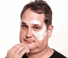 a man with white paint on his face holds a sponge to his face .