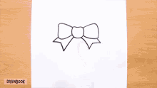 a person is drawing a bow on a piece of paper with drawbook written below it