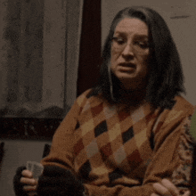a woman wearing glasses and a plaid sweater is sitting in a dark room