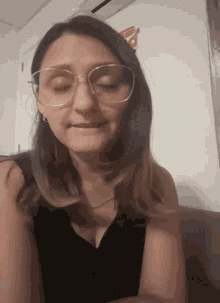 a woman wearing glasses and a black shirt looks down with her eyes closed