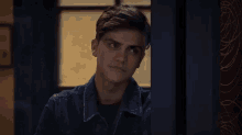 a young man in a denim jacket is standing in front of a door .