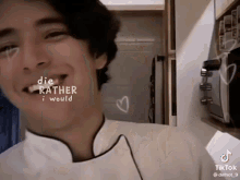 a young man in a chef 's uniform is smiling in a kitchen with a heart drawn on his face .