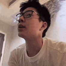 a young man wearing glasses and a white shirt looks up