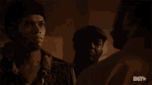a man in a hat is talking to another man with a bet logo in the corner