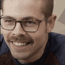 a man wearing glasses and a mustache is smiling