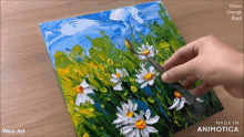 a person is painting a field of daisies on a canvas