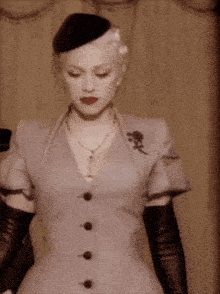 a woman wearing a grey dress and black gloves is standing in front of a curtain