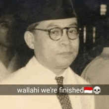 a man wearing glasses , a hat and a tie is standing in front of a skull .