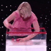 a woman in a pink shirt is standing in a tank of water holding a red object .