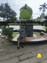 a man sits in front of a statue that says santay dulu bossque on it