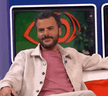 a man with a beard is sitting on a couch in front of a television and smiling .