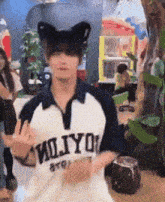 a young man wearing a cat ear hat and a shirt that says miliyo is dancing in a room .