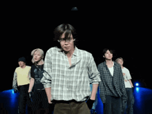 a group of young men are dancing on a stage and one of them is wearing a plaid shirt with the letter m on it